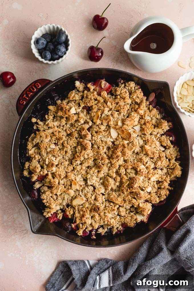 Healthy cherry crisp baked up in a cast iron skillet and resting on a pink surface.