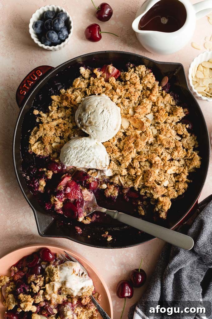 Fresh cherry crisp in a skillet being scooped onto pink plates.