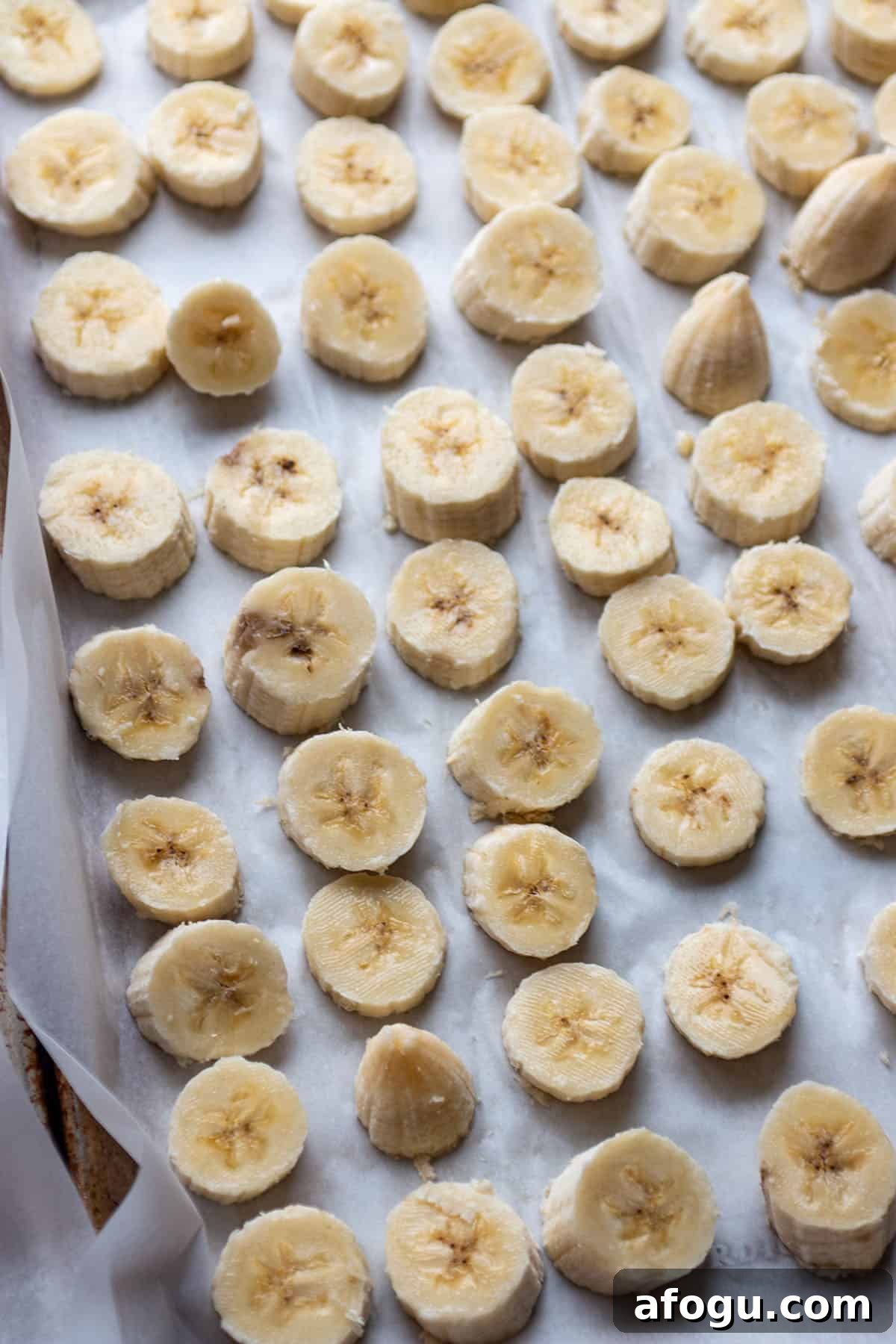 A baking sheet with some parchment paper and sliced of bananas. 