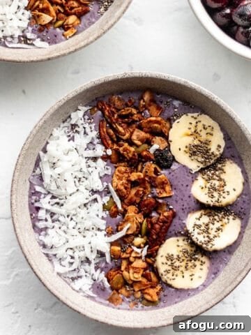 A bowl with a purple smoothie topped with coconut, granola, and banana slices.