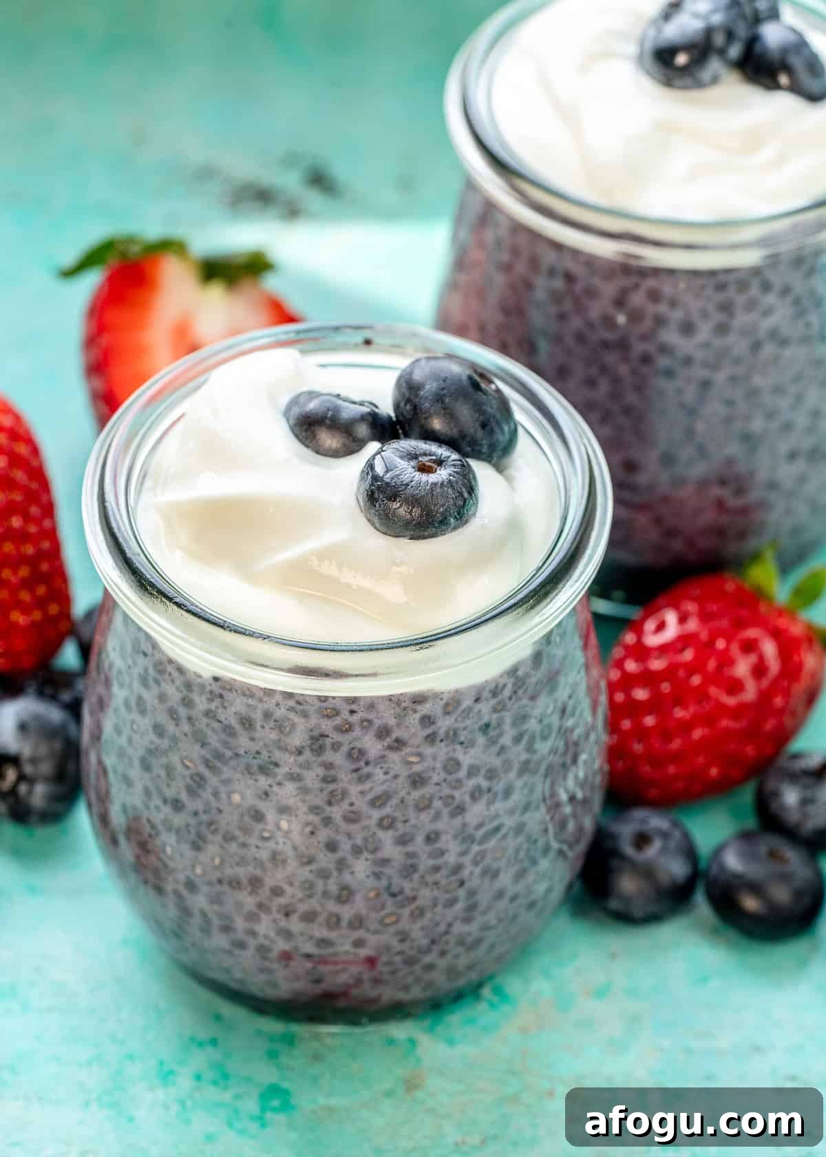 two chia blueberry pudding jars on a counter with berries