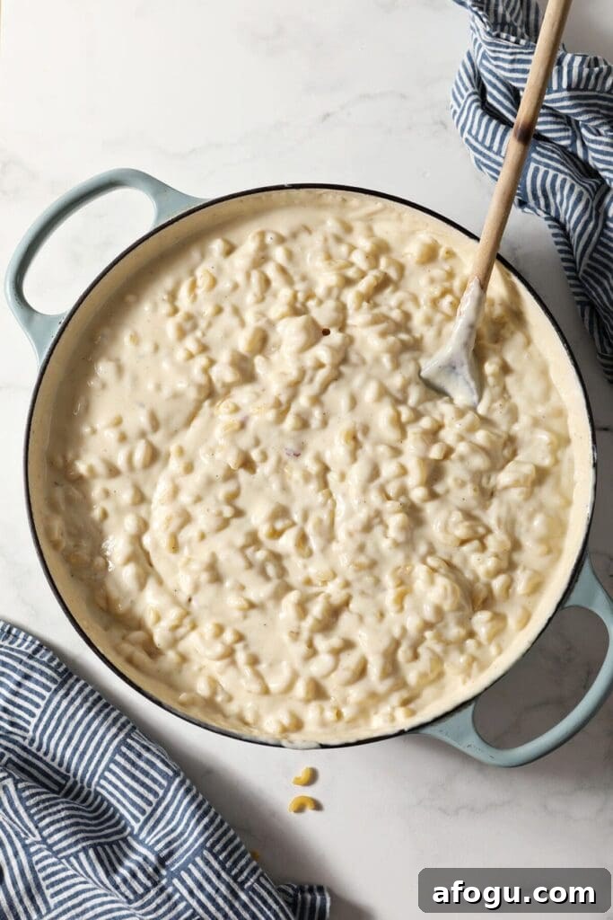 Homemade macaroni and cheese in a braiser pan with a wooden spoon inside it on marble next to patterned blue napkins