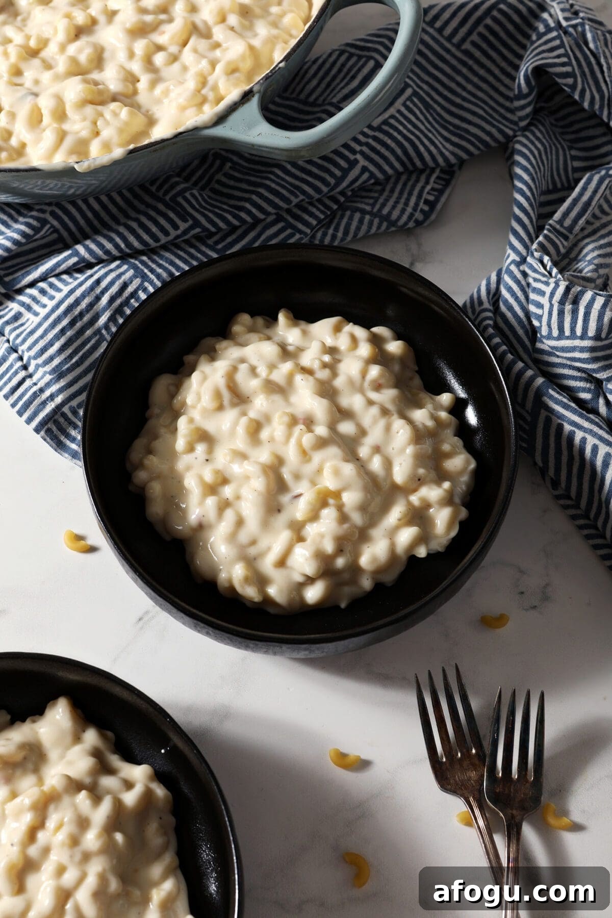 Two black bowls hold a serving of Three Cheese Mac and Cheese next to patterned blue napkins