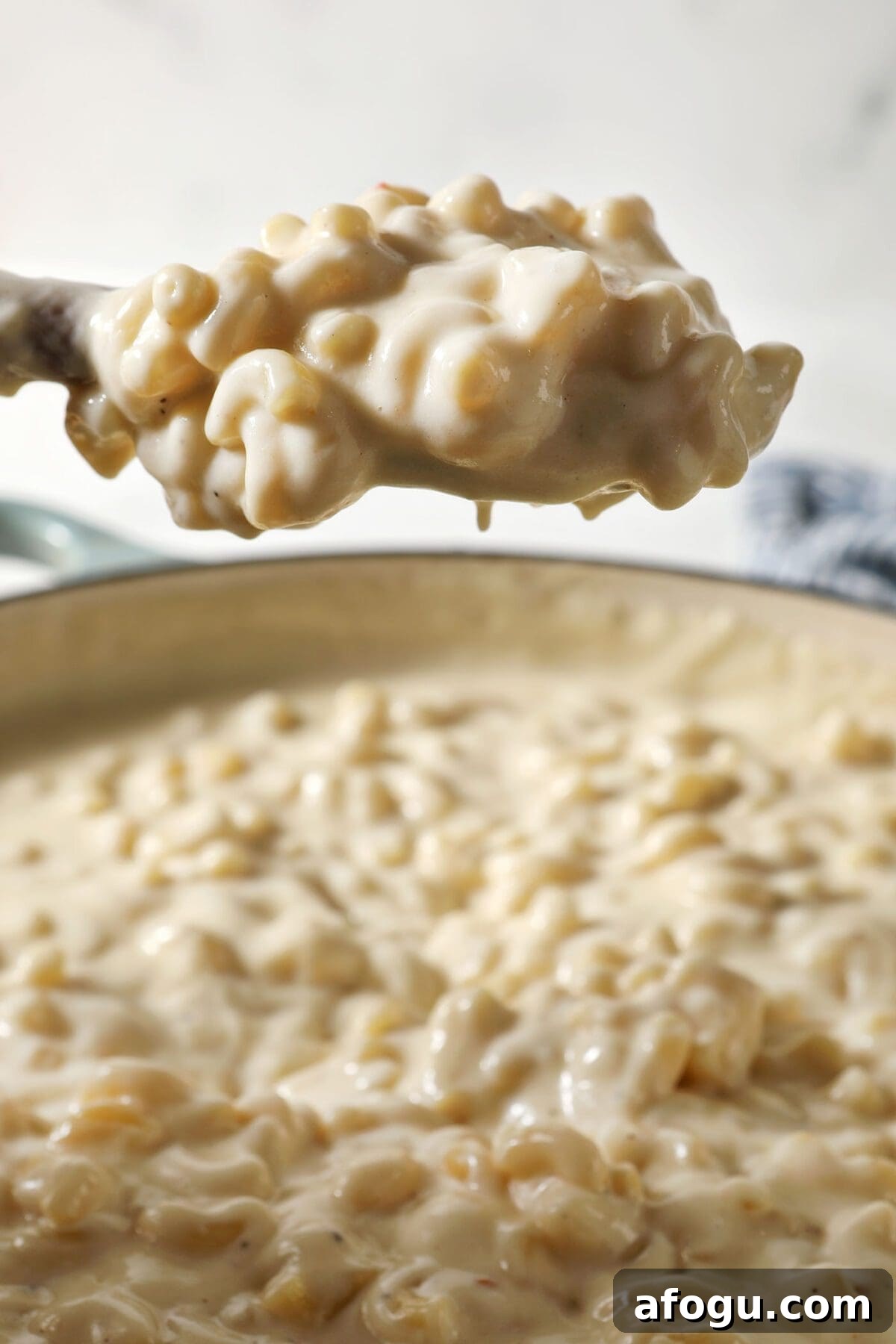 A wooden spoon lifts a serving of macaroni and cheese out of a braiser pan