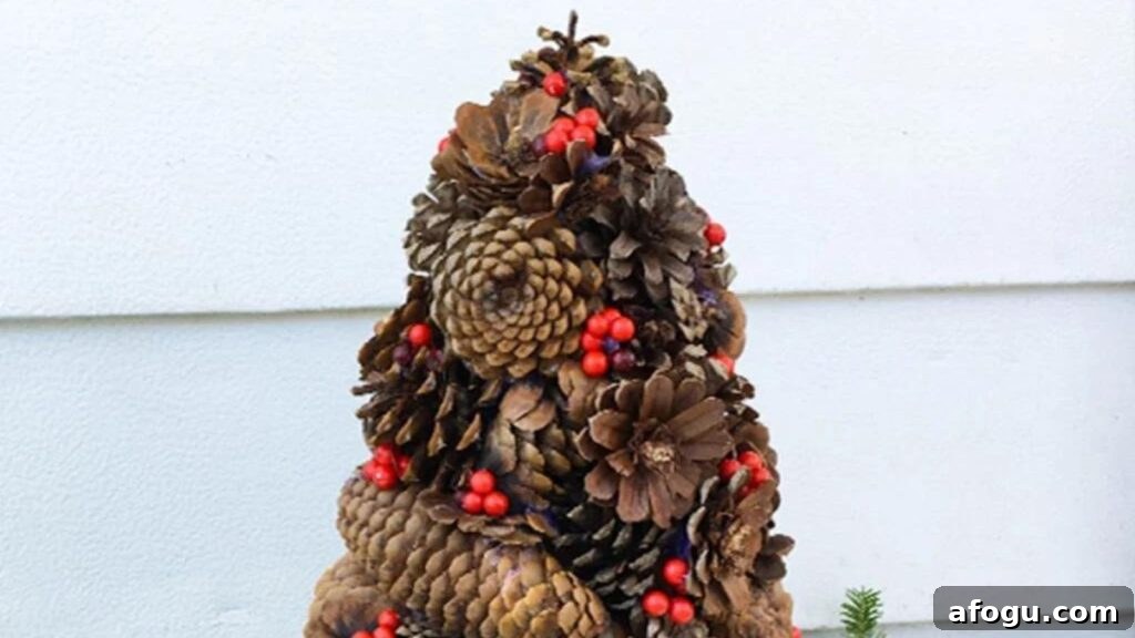 15 Pine Cone Crafts for Rustic Home Decor and Seasonal DIY 13 Square feature photo of a Christmas tree made from different varieties of pine cones decorated with red berries.