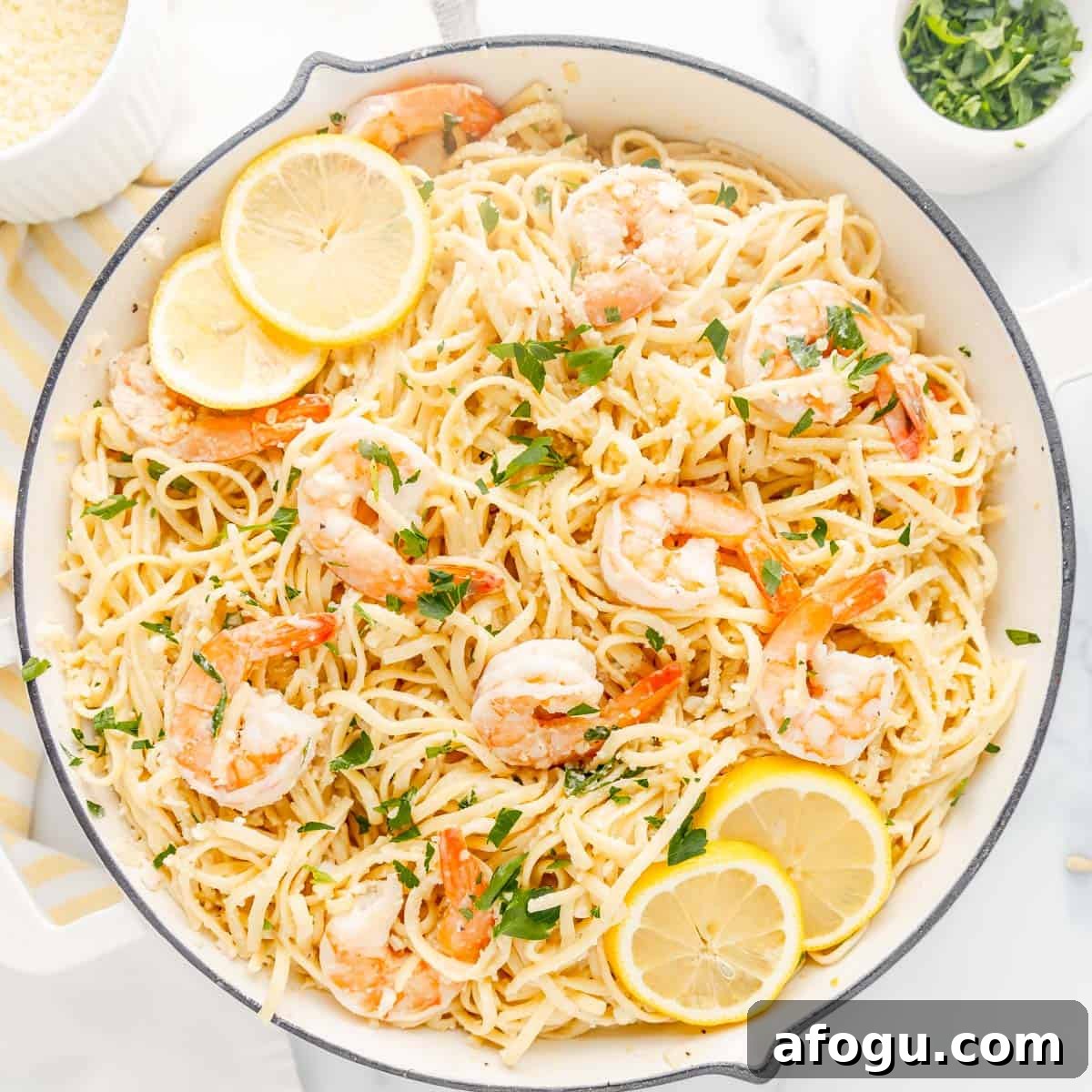 A skillet of shrimp scampi with spaghetti, garnished with lemon slices and parsley.