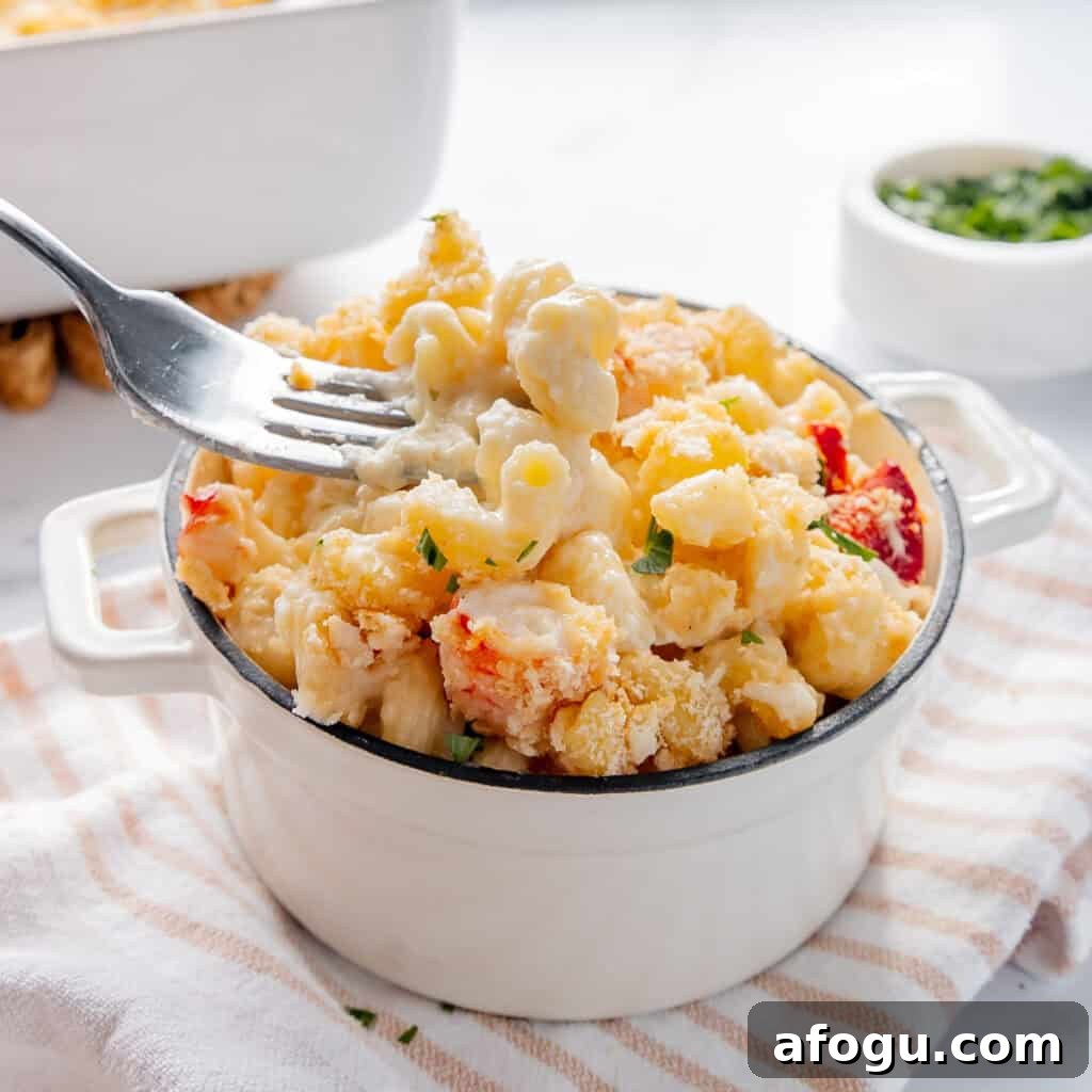 A fork lifting a portion of creamy lobster mac and cheese from a white dish on a striped cloth.