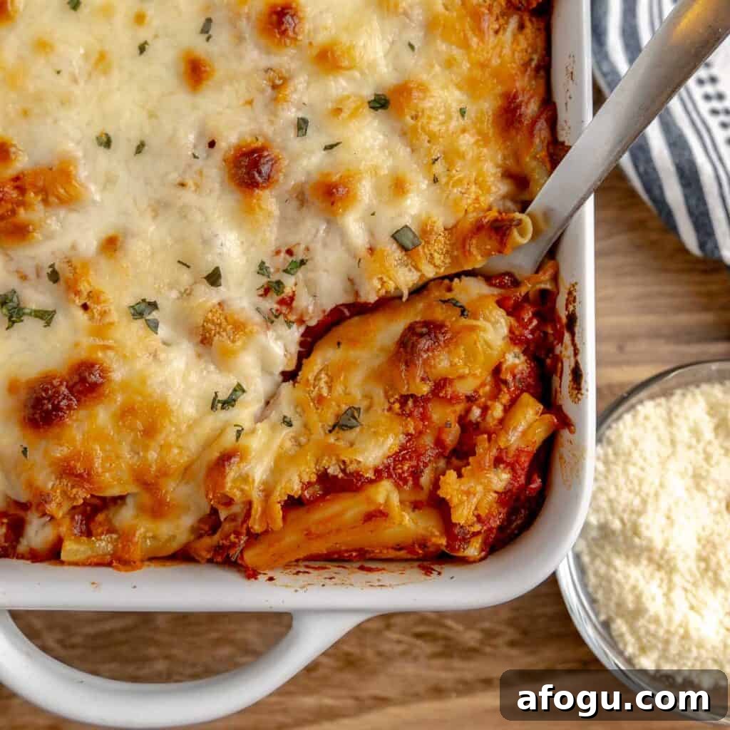 A pan of baked ziti with a spoon and parmesan cheese.