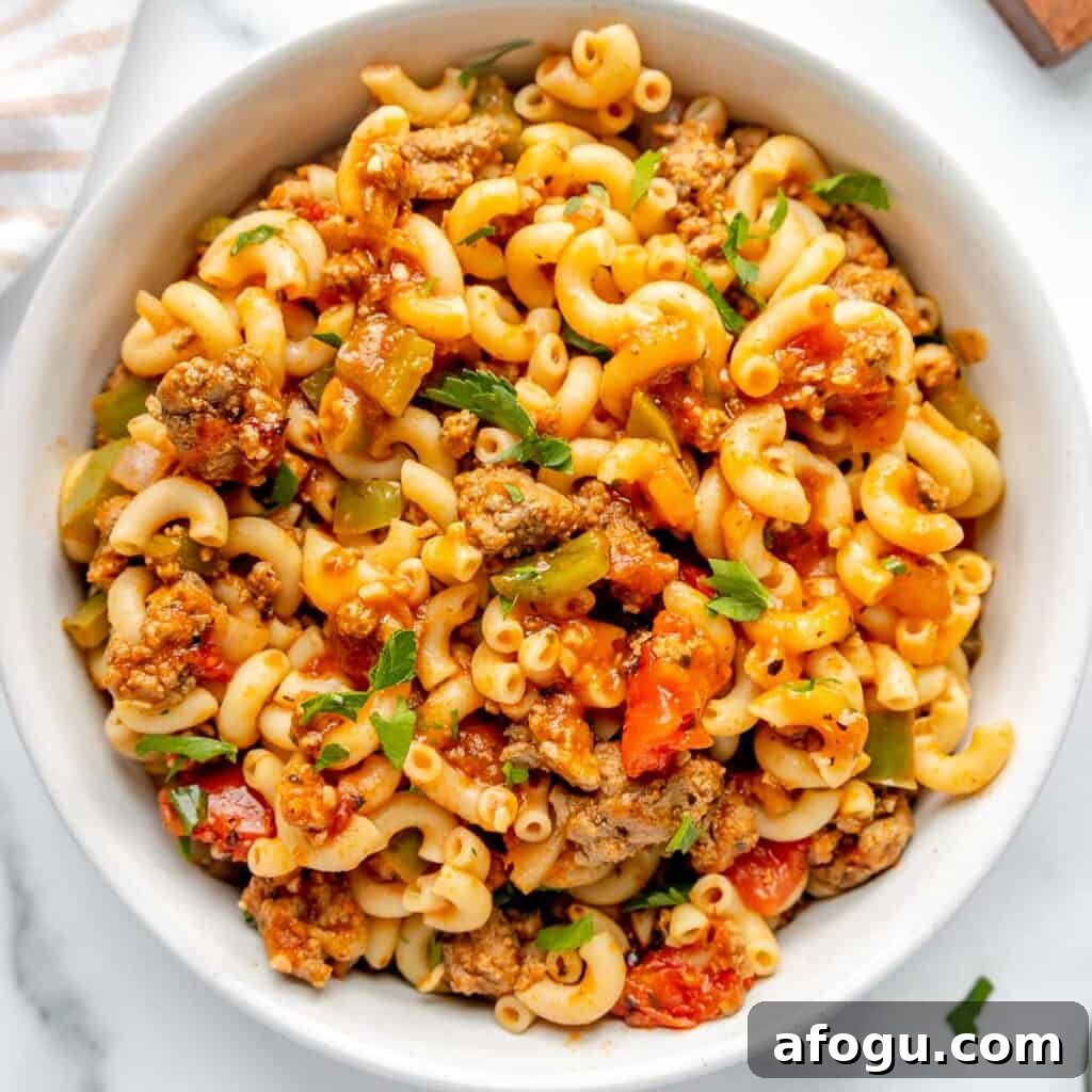A bowl filled with macaroni pasta mixed with ground meat, diced tomatoes, green bell peppers, and garnished with parsley.