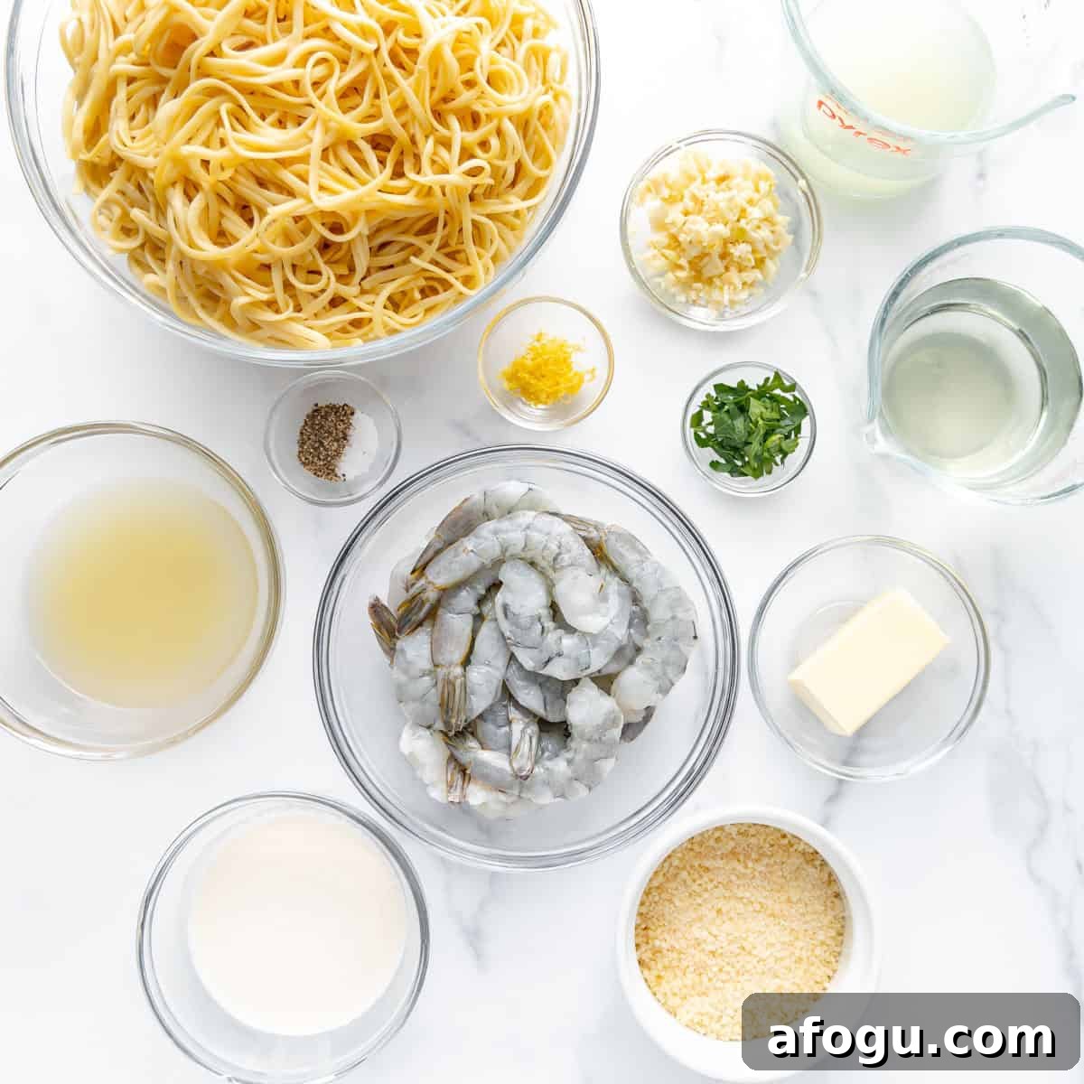 Ingredients for a pasta dish are arranged: cooked pasta, raw shrimp, garlic, lemon zest, parsley, white wine, parmesan, pasta water, cream, butter, pepper, and lemon juice.