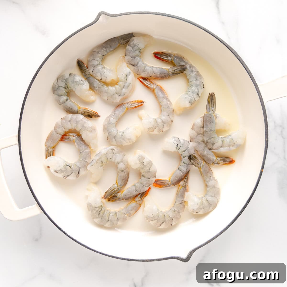 Raw shrimp arranged in a white pan on a white marble surface.