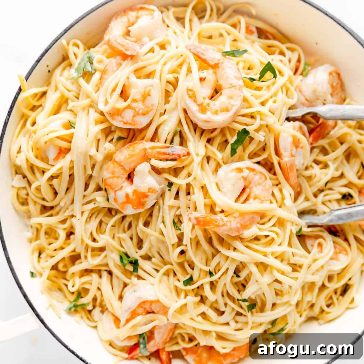 A pan of cooked spaghetti mixed with shrimp and garnished with fresh herbs.