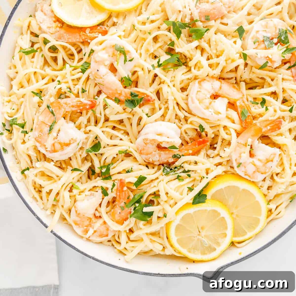 A dish of shrimp pasta with lemon slices and parsley garnish in a white bowl.