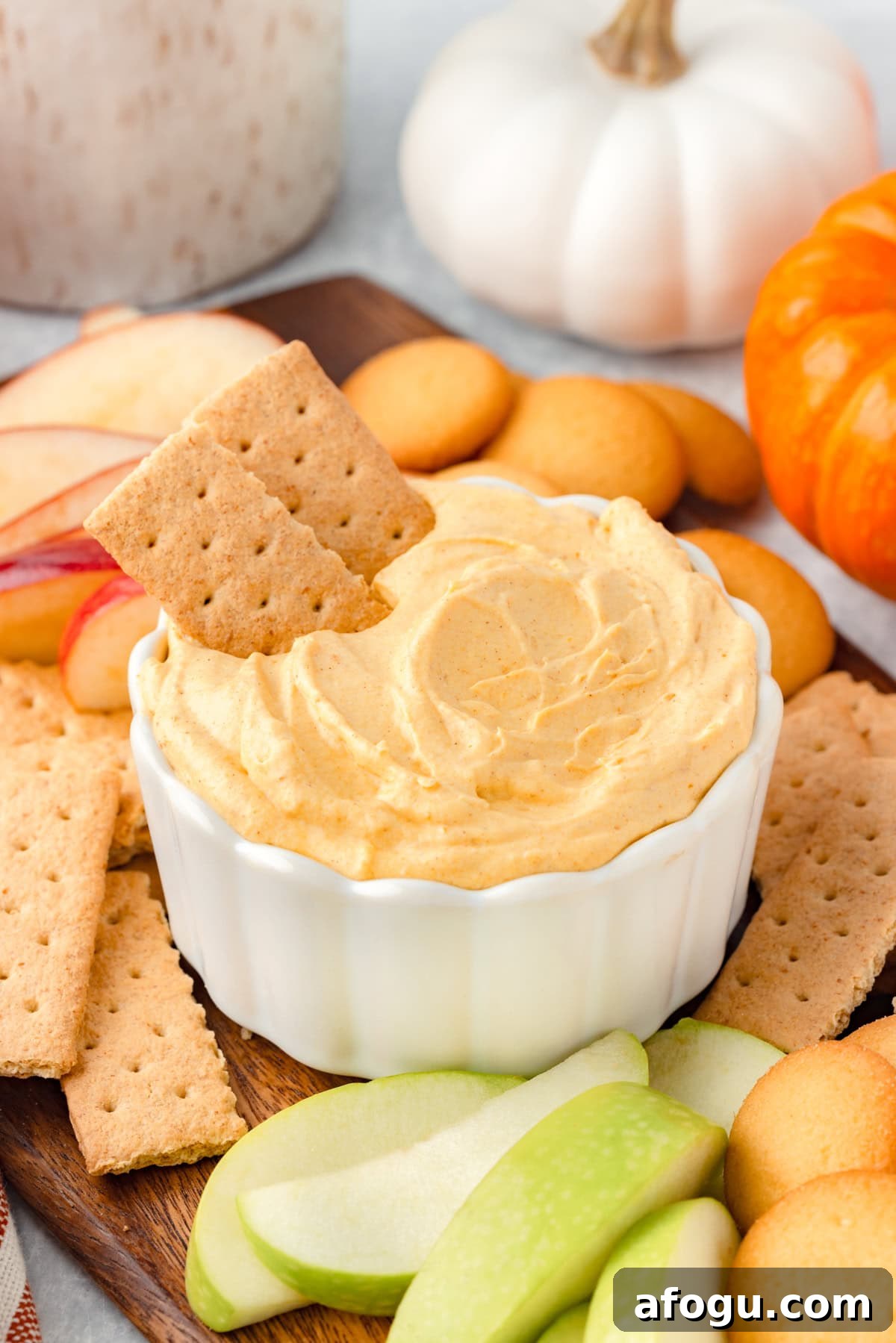 A white bowl filled with pumpkin dip, topped with two graham crackers on the side.