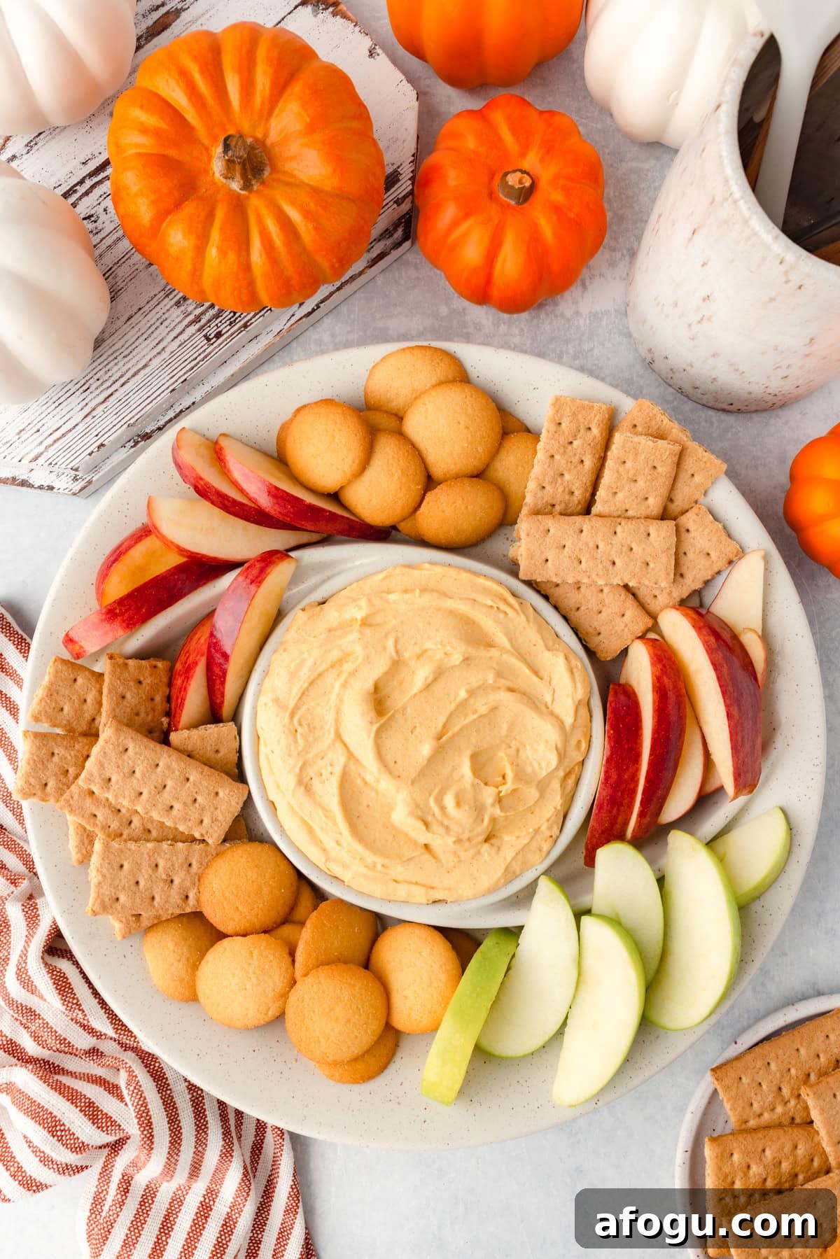 A plate of pumpkin dip is surrounded by apple slices, graham crackers, and vanilla wafer cookies.