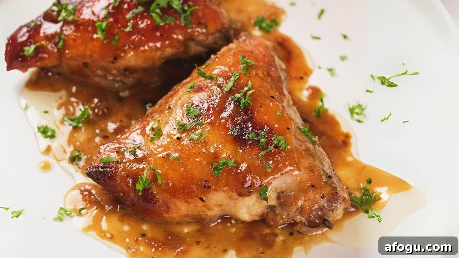 Two apricot chicken thighs on a plate, topped with chopped herbs and surrounded by a light brown sauce.