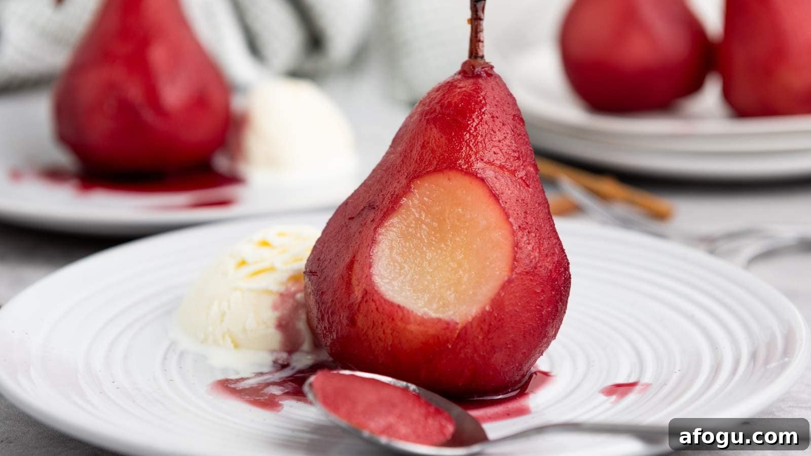 A poached pear with a section scooped, served with a scoop of vanilla ice cream and sauce on a white plate, with a spoon in front.