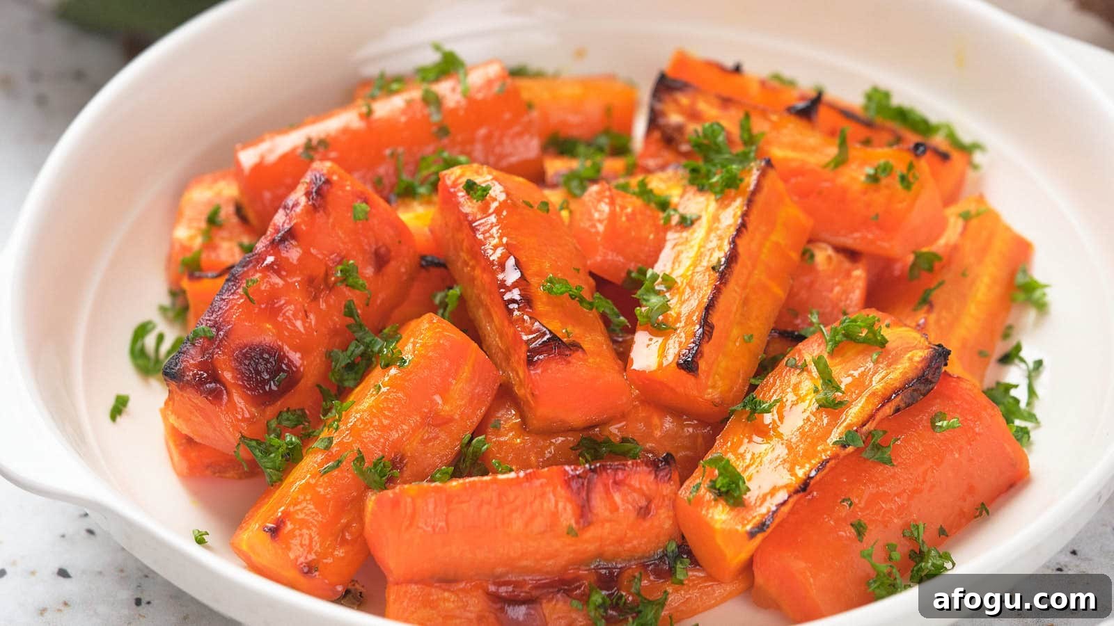 Honey roasted carrots garnished with chopped parsley in a white dish.
