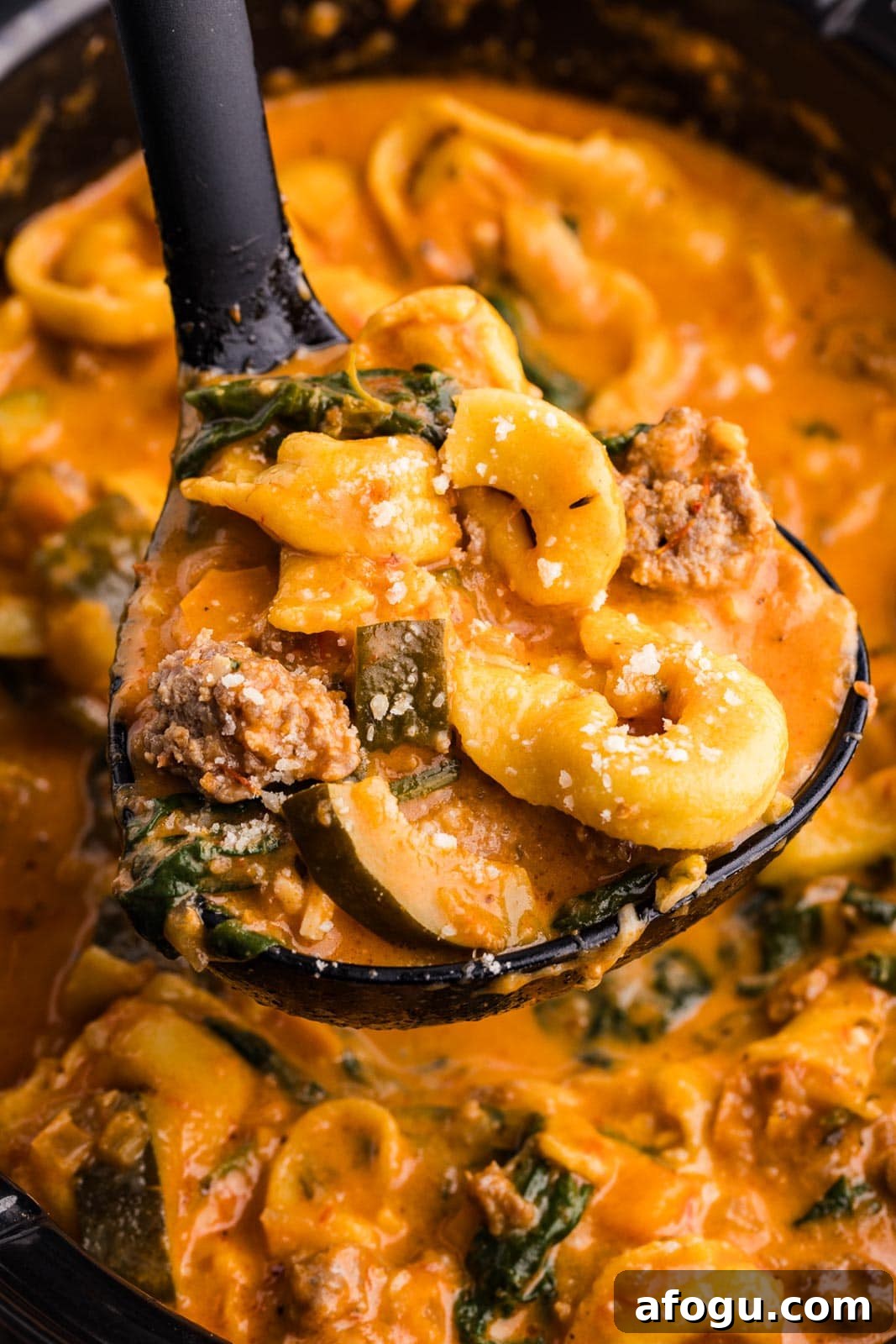 closeup view of black ladle containing tortellini soup with slow cooker of soup in background