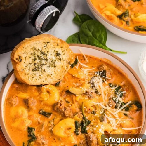 two bowls of tortellini soup, one with garlic bread on side, with black slow cooker in background
