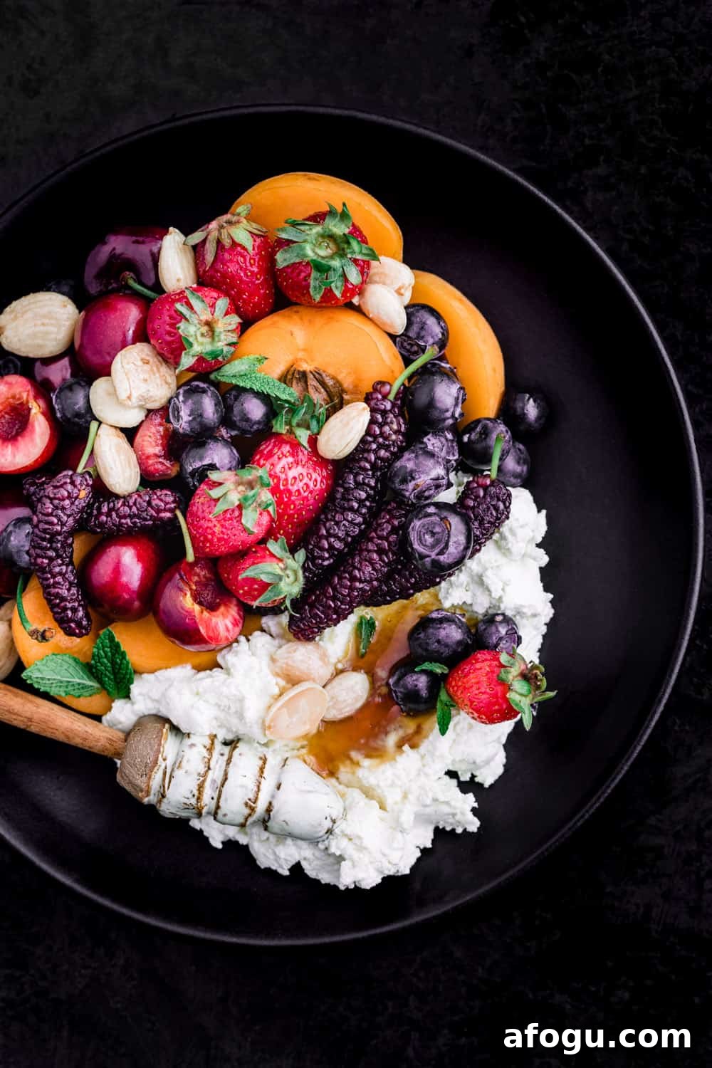 Summer Salad Recipe That Keeps Giving All Season Long 14 Summer fruit with fresh cheese, almonds and honey on a black plate; overhead shot on a black background.