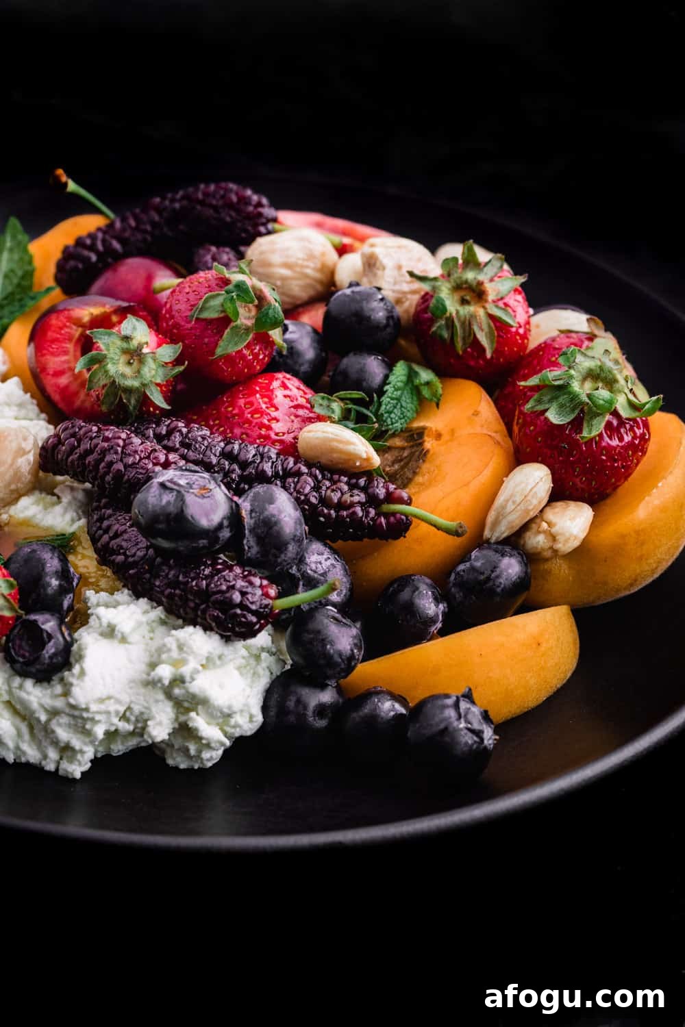 Summer Salad Recipe That Keeps Giving All Season Long 15 Single angle shot of Summer fruit with fresh cheese, almonds and honey on a black plate and background.