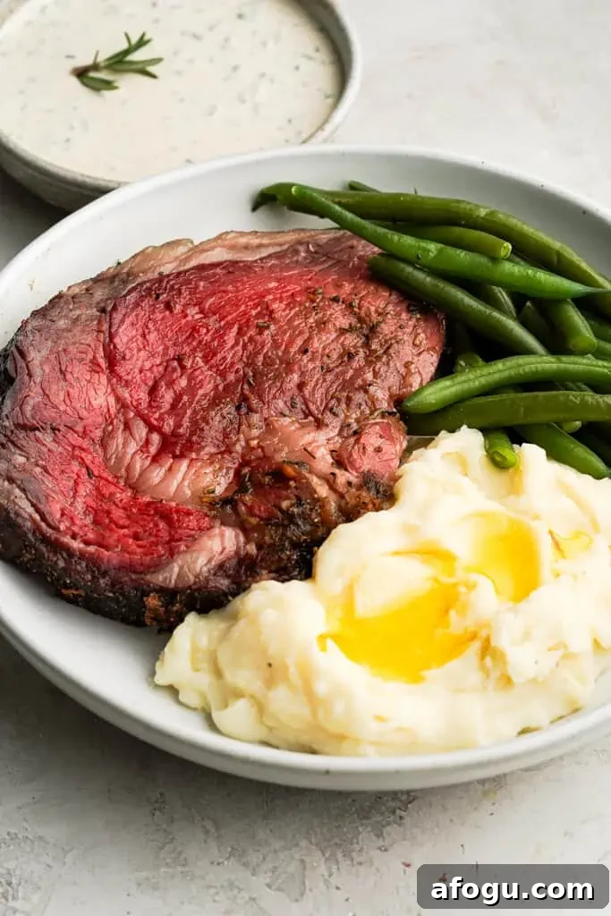 plated prime rib roast with a side of mashed potatoes and green beans with a bowl of horseradish cream in the background
