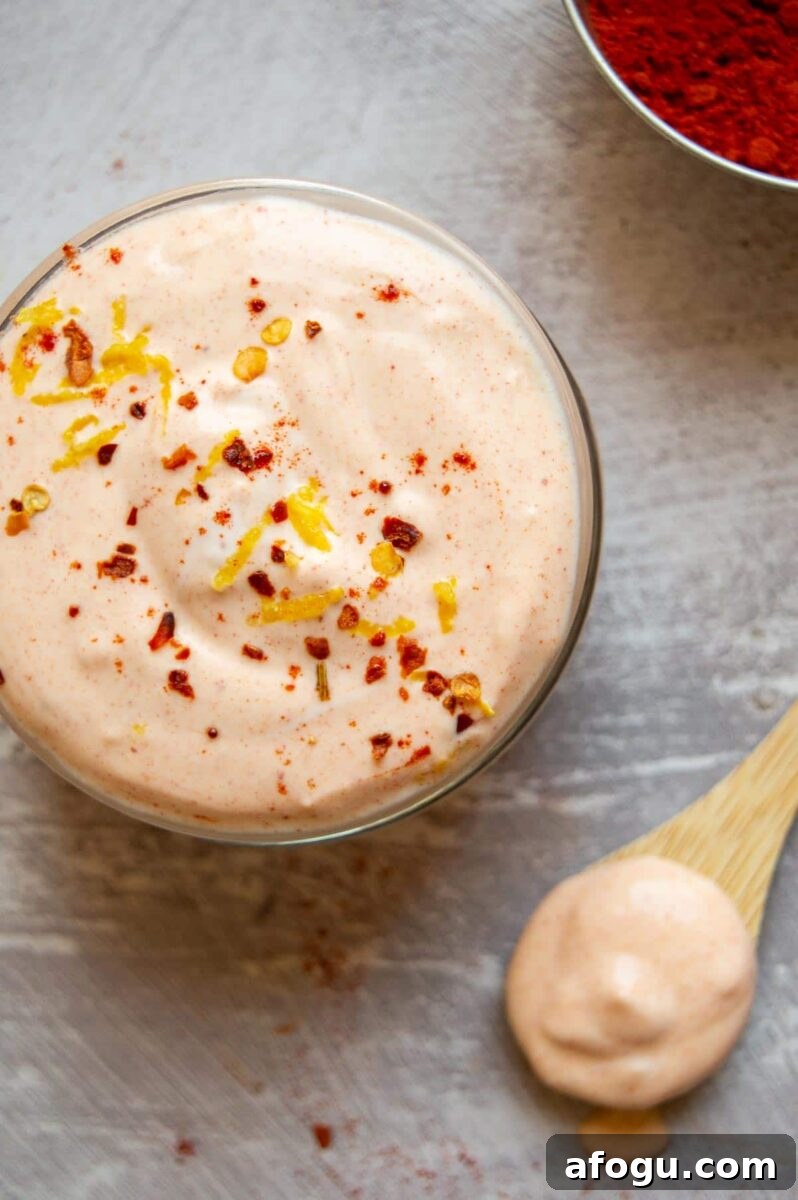 Top down view of a glass jar of thick creamy pale orange sauce with chili flakes sprinkled over.