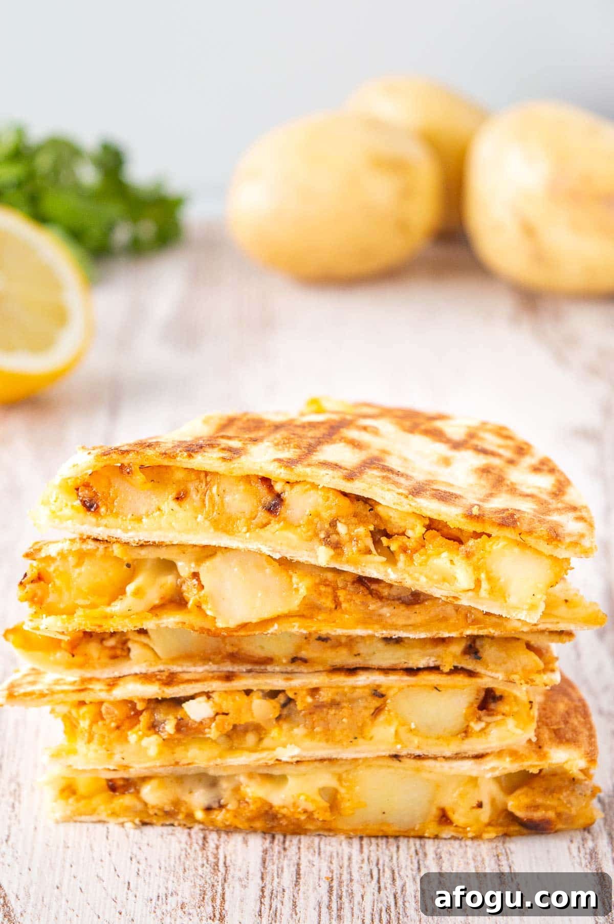 A stack of five cheesy potato quesadillas on white wood.