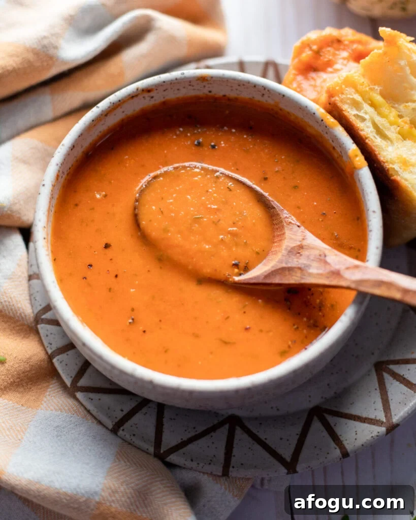 vegan creamy tomato soup in a white bowl with a wooden spoon and grilled cheese.
