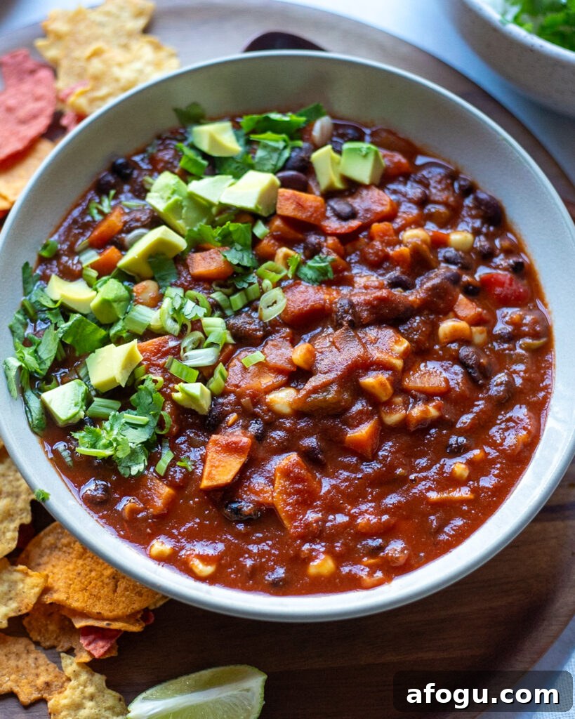 close up view of a bowl of black bean and sweet potato chili topped with avocado and cilantro