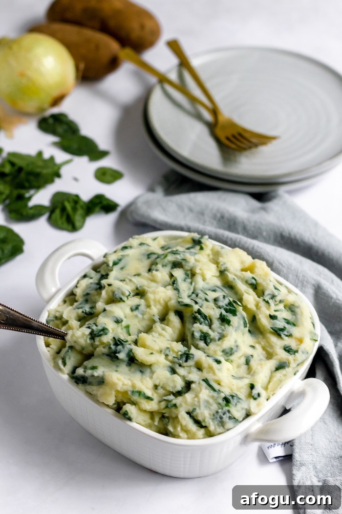 Images shows a dish of spinach mashed potatoes on a table next to an empty plate