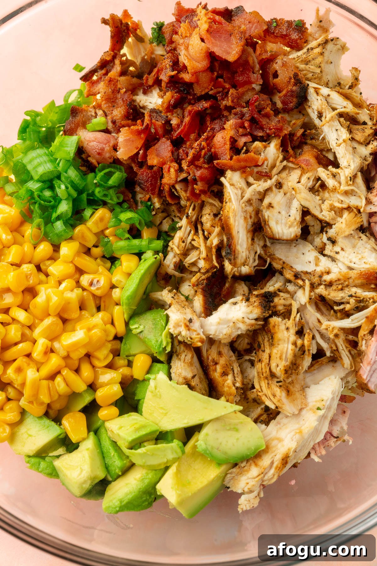 Cooked chicken, avocado, corn, green onions and bacon in a large mixing bowl not yet mixed together.