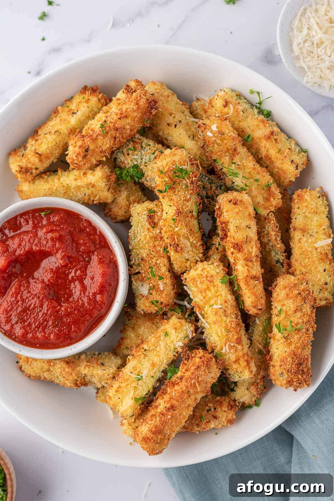 Air fryer zucchini sticks on a plate with a bowl of marinara.