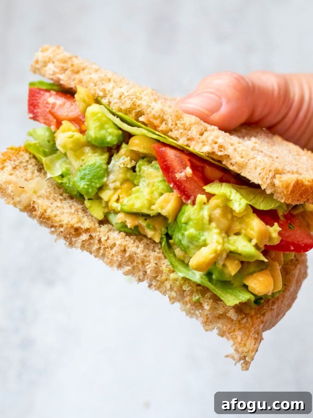 Chickpea Avocado Salad on wheat bread topped with tomatoes and lettuce.