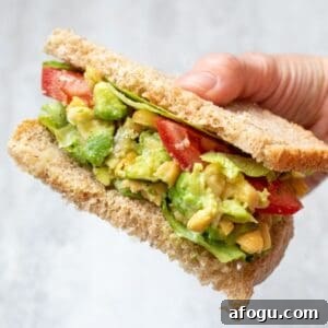Chickpea Avocado Salad on wheat bread topped with tomatoes and lettuce.