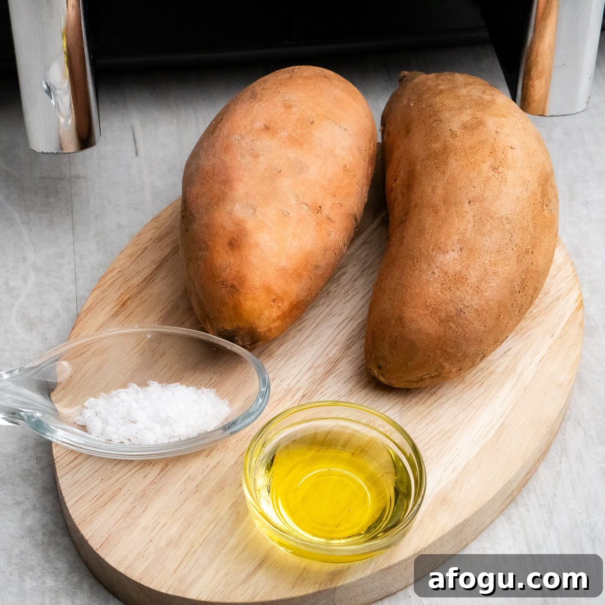 Two Sweet potatoes, olive oil and salt in glass dishes on a chopping board