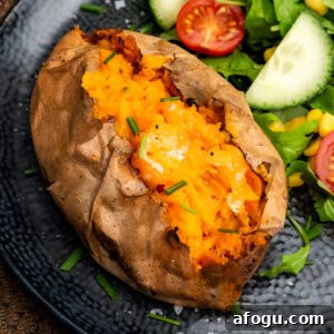 Jacket Sweet Potato in the air fryer cut open with chopped chives on top and a salad on the side