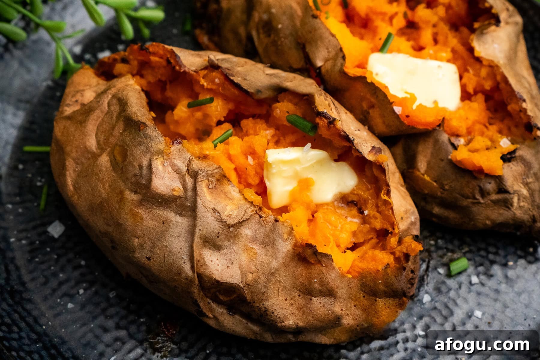 Two Air fryer Sweet Potatoes cut open with butter on top and chopped chives