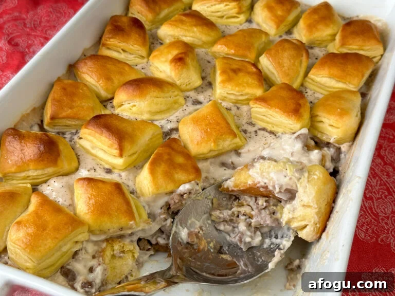 Large silver serving spoon in a 9 x 13 dish of biscuit and country gravy breakfast casserole with three easy layers on a red napkin.