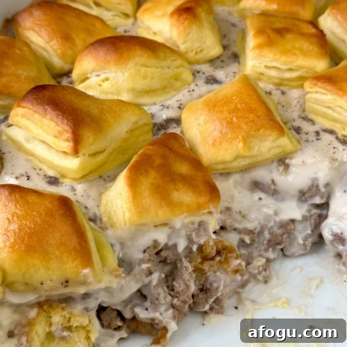 Close up Biscuit and Gravy Casserole showing layers of baked biscuits, crumbled pork sausage and country sausage gravy in a 9 x 13 casserole dish.