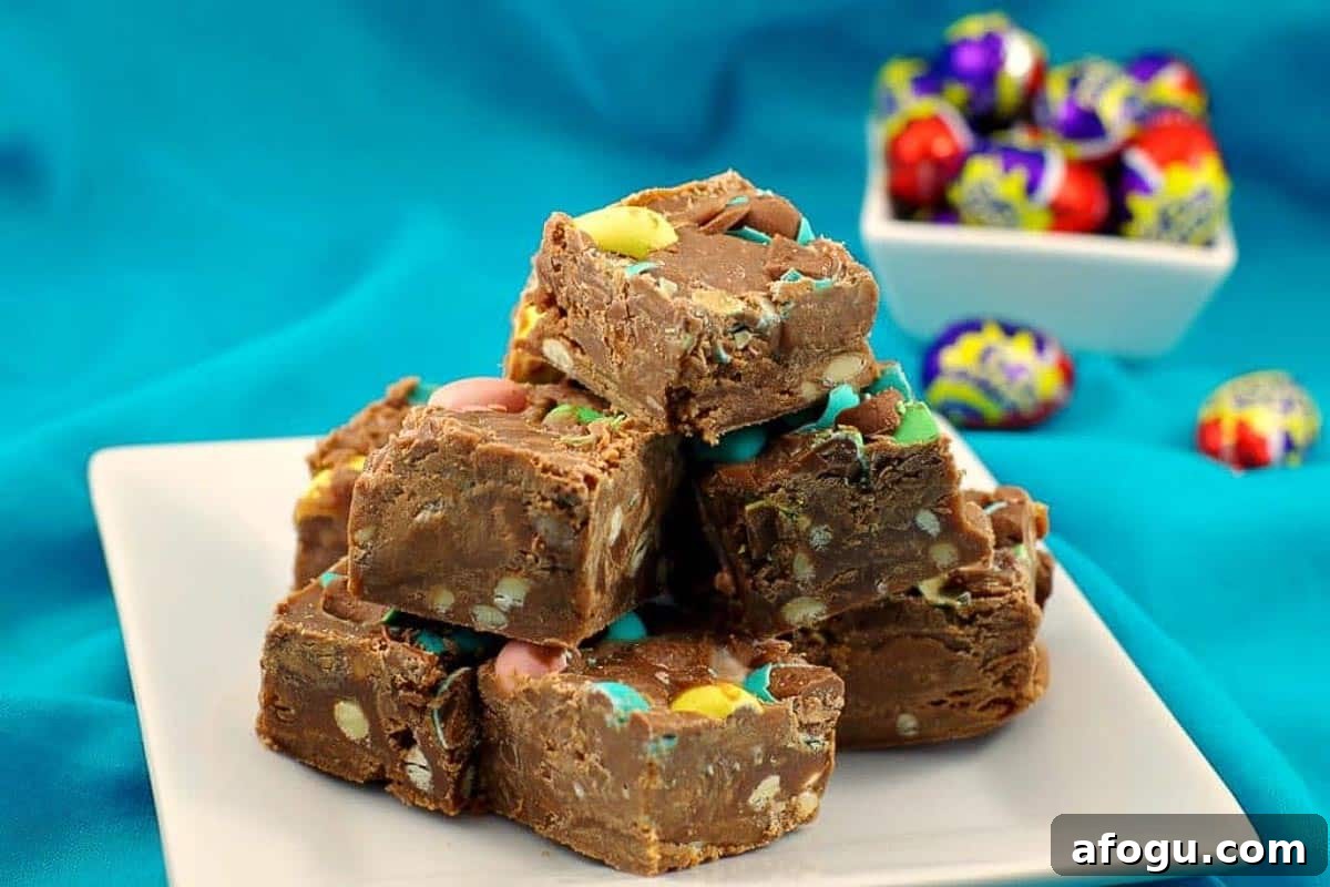 Microwave Easter Egg Fudge stacked on a white plate with a bowl of Cadbury Mini Easter Creme eggs in the background.