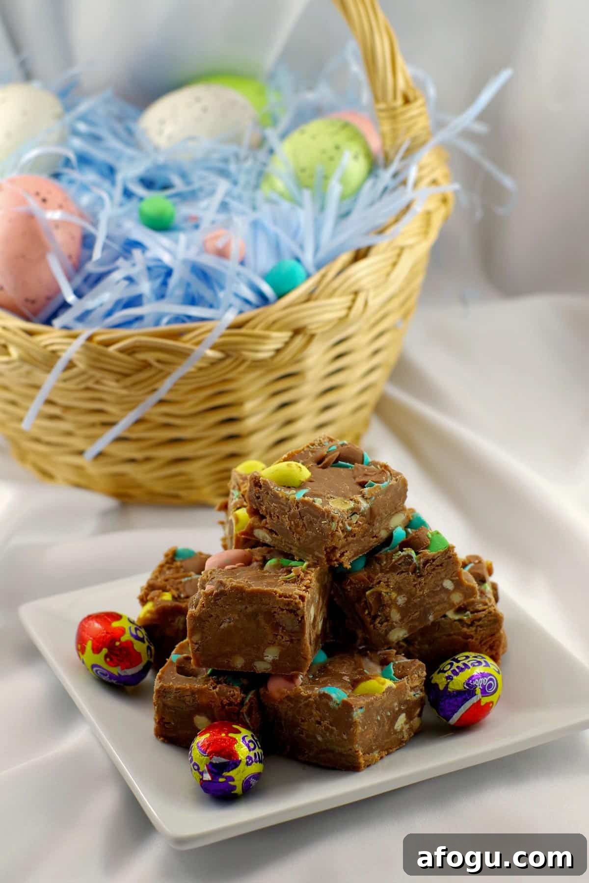 Easter Egg Fudge stacked on a white plate with a Easter basket with eggs in the background.