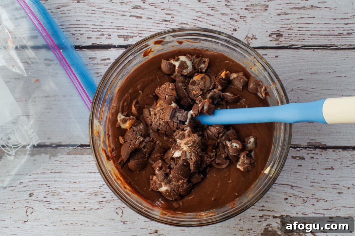 Mini eggs mixed in with melted chocolate in a glass bowl with a spatula.