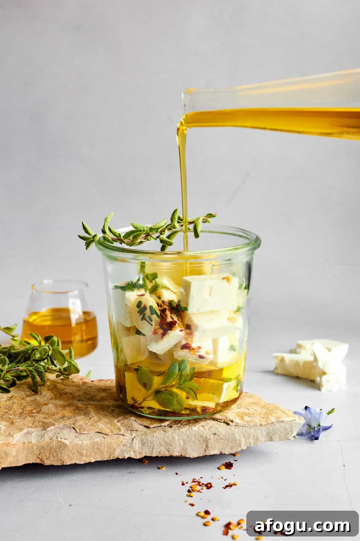 Marinade being poured over feta cubes in a glass container.