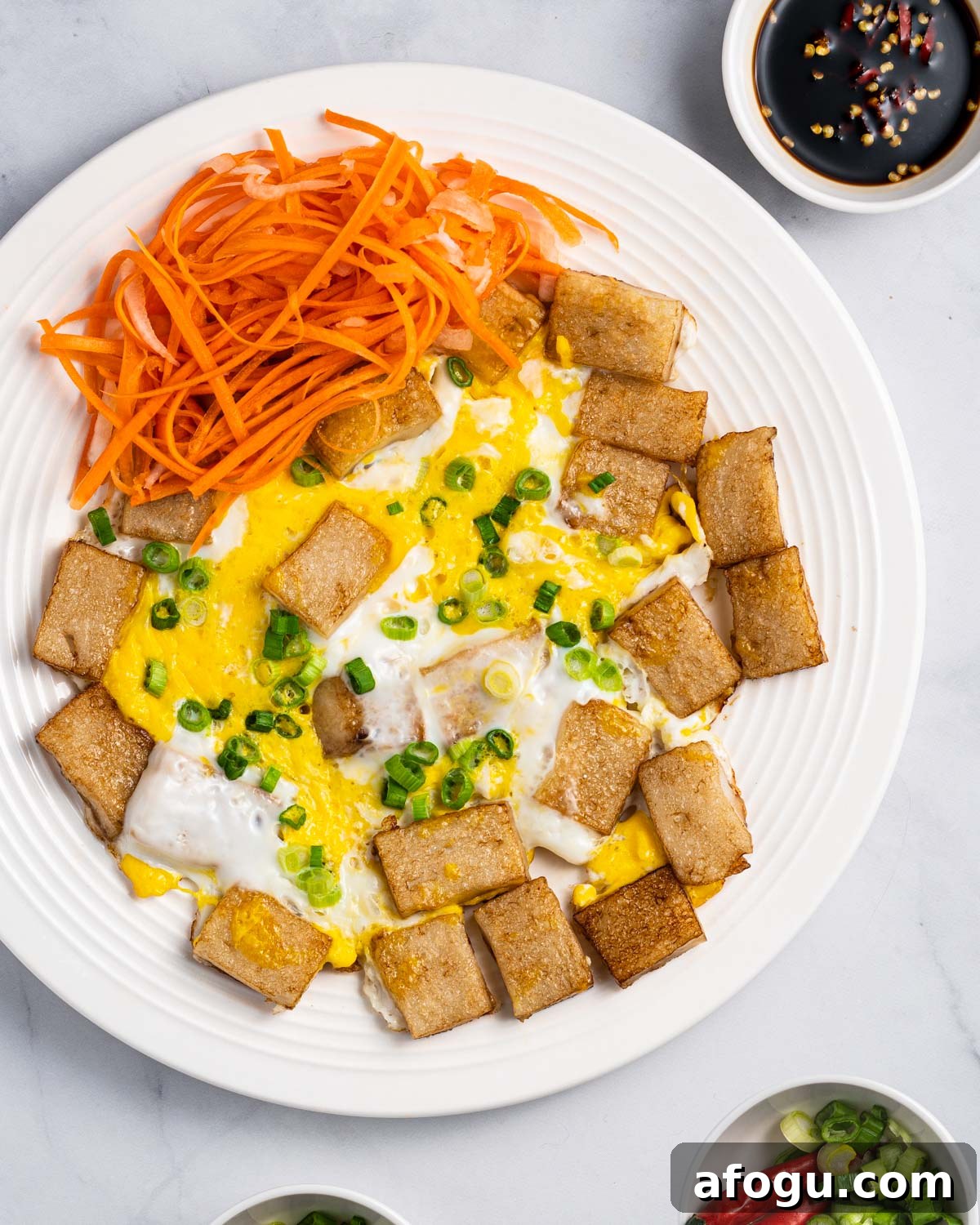 Plate of bot chien (Vietnamese fried rice cakes) with sides of pickled carrots and daikon, dipping sauce, chopped scallions, and red peppers.