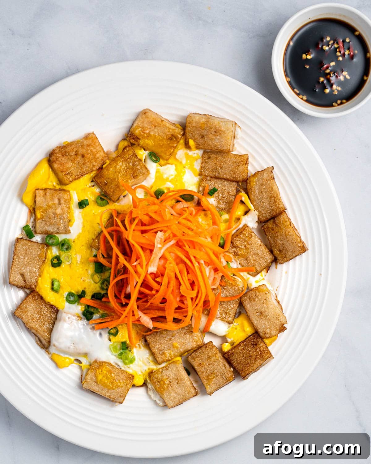 A plate of bot chien with pickled carrots and daikon on top and dipping sauce on the side.