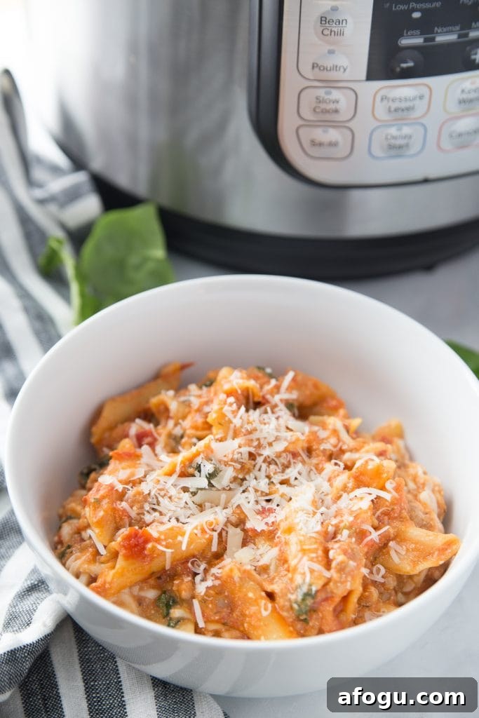 White bowl of bake ziti topped with cheese with an Instant Pot in the background 