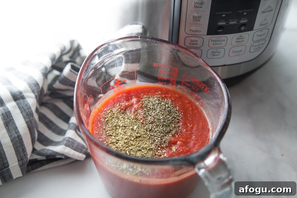 Clear glass measuring cup with tomato sauce and dried herbs in front of an Instant Pot on a marble countertop