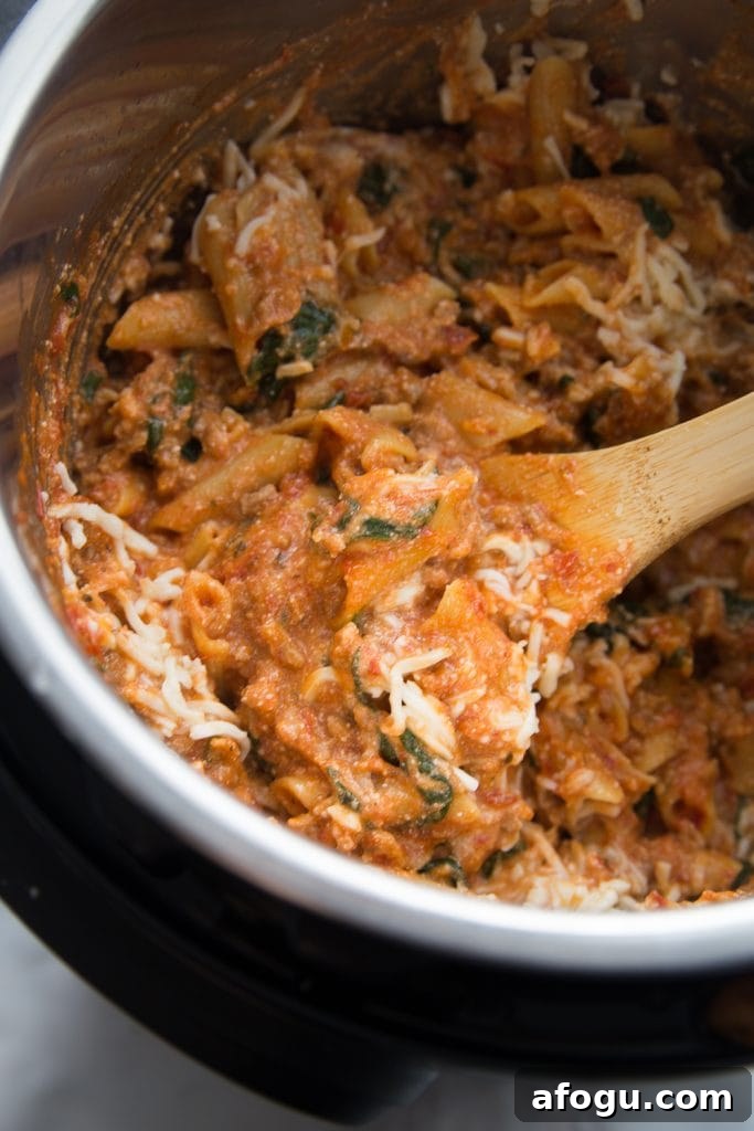 Instant Pot cooked baked ziti and lots of melty cheese...pasta being stirred with a wooden spoon. 